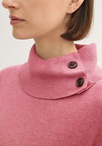 Rosa Rollkragensweater mit einem gerippten Kragen und zwei dunkelbraunen Knöpfen am Kragen, hergestellt aus einem weichen Strickmaterial.
