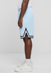Lyseblå atletiske shorts med sorte og hvide detaljer, der har et delt kantdesign. Båret med hvide sneakers og ankelsokker.
