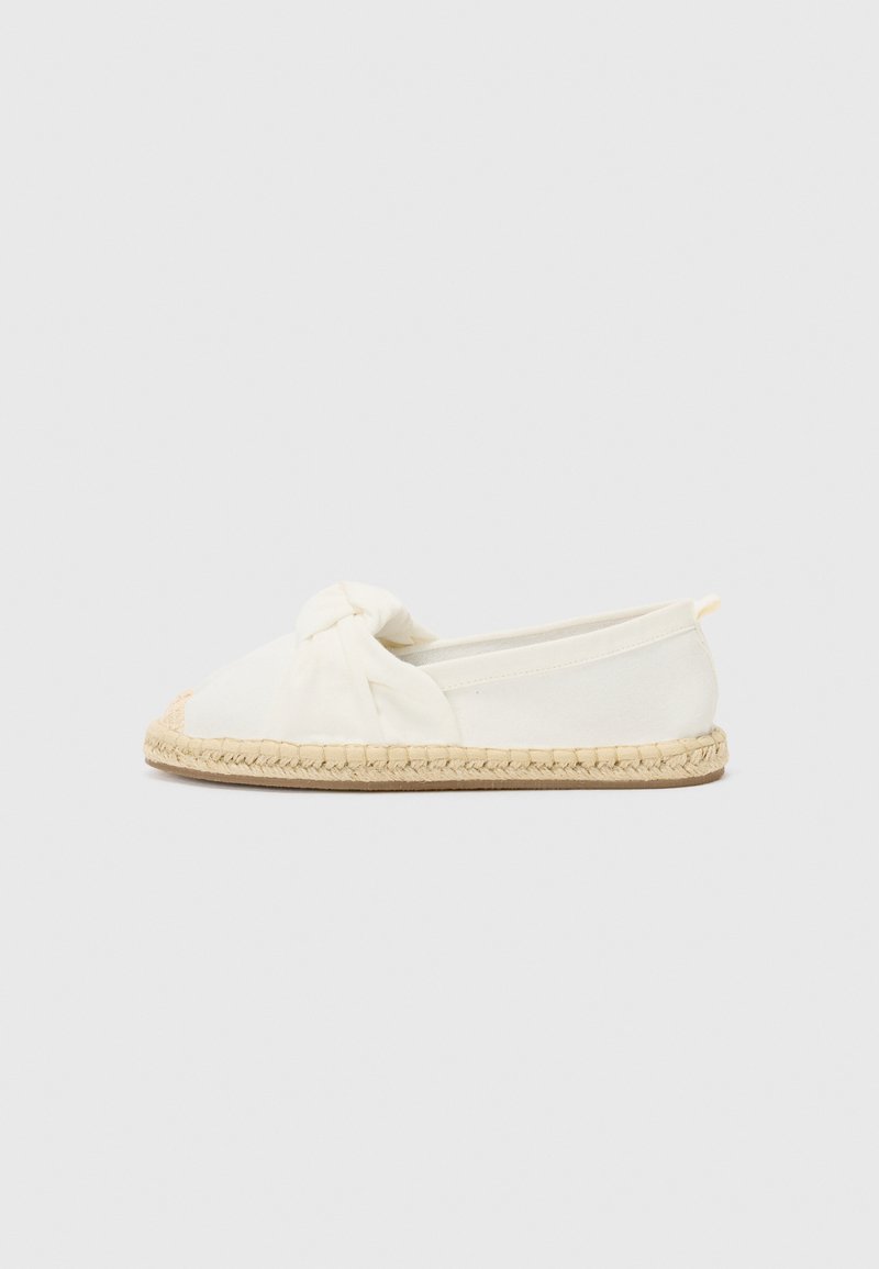 Sapatilha de lona branca, tipo slip-on, com detalhe frontal em nó, sola em corda de juta e design minimalista. Forma plana com bico arredondado.
