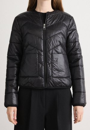 Kobieta nosząca czarną, pikowaną kurtkę na zamek z dwoma przednimi kieszeniami i długimi rękawami, w połączeniu z czarnymi spodniami.