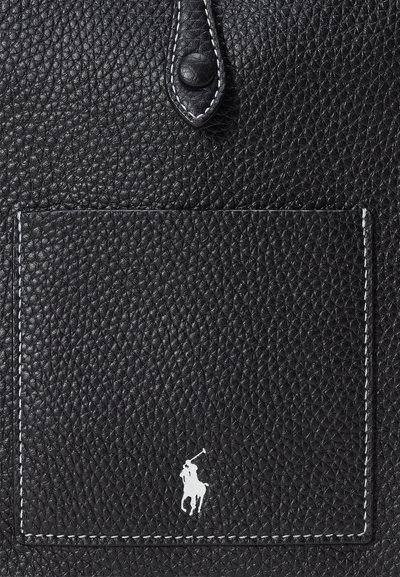 Μαύρη δερμάτινη τσάντα με υφή, που διαθέτει μπροστινή τσέπη και λευκό λογότυπο. Οι ραφές είναι σε αντίθεση με την ανθεκτική κλειστή κορυφή.