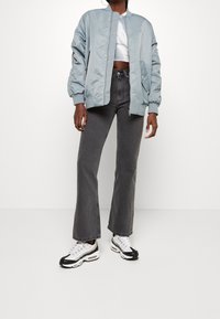 Giacca bomber azzurro chiaro con polsini elasticizzati, abbinata a jeans a zampa d'elefante grigio scuro a vita alta e sneaker bianco-neri con dettagli in rete.