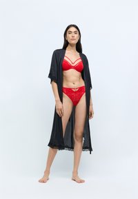 Černý krajkový kimono župan vrstvený přes červenou krajkovou podprsenku a odpovídající tangách, zdobený složitými vzory a zlatými akcenty na spodním prádle.