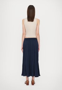 Beige top bez rukávů a námořnická maxi sukně s plisováním. Sukně má elastický pas a volný siluetu. Hnědé boty na podpatku.