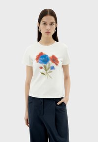 Witte katoenen T-shirt met een kleurrijke bloemenprint van blauwe en rode bloemen. Het ontwerp is zacht en mengt goed, met een relaxte pasvorm.