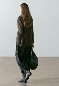 Brown wool blazer with flared sleeves, paired with black wide-leg trousers and black ankle boots. Carrying a black bag. Neutral background.