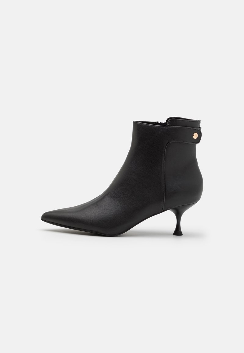 Bottine en cuir noir avec bout pointu, talon kitten, fermeture éclair latérale et petit détail bouton en métal près du bord supérieur.