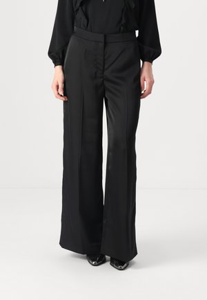 Pantaloni neri a gamba larga in tessuto morbido con un design sartoriale, featuring una vita alta e dettagli minimi. Abbinati a scarpe con punta.