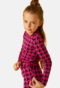Top de manga larga rosa y leggings con un patrón de espiga negro. La tela parece elástica y cuenta con un cordón en la cintura.