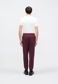 Μπορντό παντελόνια τύπου jogger με ριμπ μανσέτες και πίσω τσέπη, συνδυασμένα με εφαρμοστό λευκό t-shirt. Απλός σχεδιασμός, μαλακή υφή, άνετη εφαρμογή.