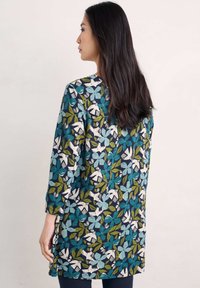 Kwiatowa tunika na ciemnoniebieskim tle, pokryta zielonymi, turkusowymi i białymi wzorami liści oraz kwiatów; długie rękawy i szczeliny po bokach.