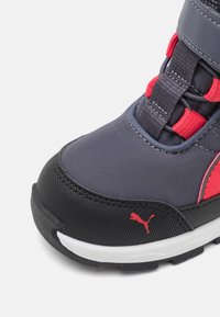 Zapatilla deportiva gris y roja con parte superior de tejido suave, suela de goma negra, cordones elásticos y logo de Puma prominente.