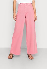 High-waisted, wide-leg jeans in soft pink denim, featuring a button closure, front pockets, and a clean hem. Accompanied by strappy sandals.