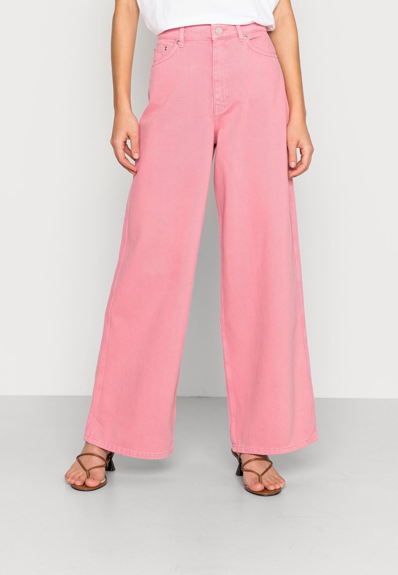 High-waisted, wide-leg jeans in soft pink denim, featuring a button closure, front pockets, and a clean hem. Accompanied by strappy sandals.