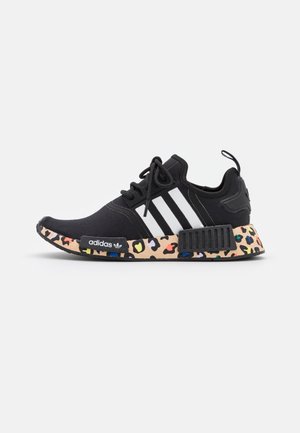Czarny sneaker Adidas z białymi paskami i wielokolorową podeszwą w lamparcie cętki, zawiązywany na sznurowadła i z pętelką na pięcie.