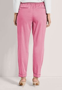 Roze, lichtgewicht taps toelopende broek met een elastische tailleband, twee achterzakken en opgerolde pijpen, gecombineerd met beige sandaalhakken.