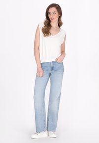 Hvid ærmeløs top med V-hals, parret med lyseblå lige ben jeans og hvide sneakers. Toppen har et tætsiddende, elastisk taljebånd.