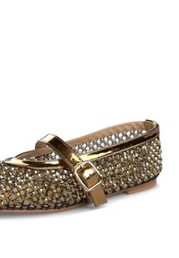 Chaussure plate avec un bout rond, présentant une finition métallique dorée et une sangle décorative avec une boucle. Ornées de petits bijoux scintillants.