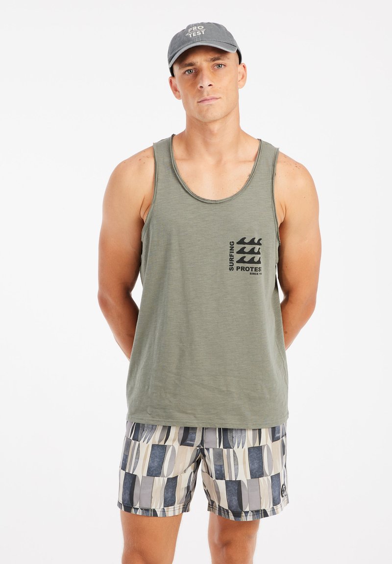Olivengroene tanktop met zwart surfprint op de borst; gecombineerd met patroon zwembroek in blauw en beige tinten, met geometrische vormen.