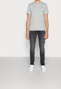 Grå bomullströja med korta ärmar och en liten logotyp, kombinerad med slim-fit, urtvätta svarta jeans och vita sneakers.