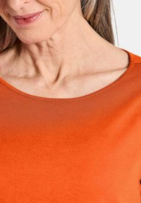 Oranges Oberteil mit rundem Ausschnitt, aus glattem Stoff gefertigt. Verfügt über ein einfaches Design und eine figurbetonte Silhouette.