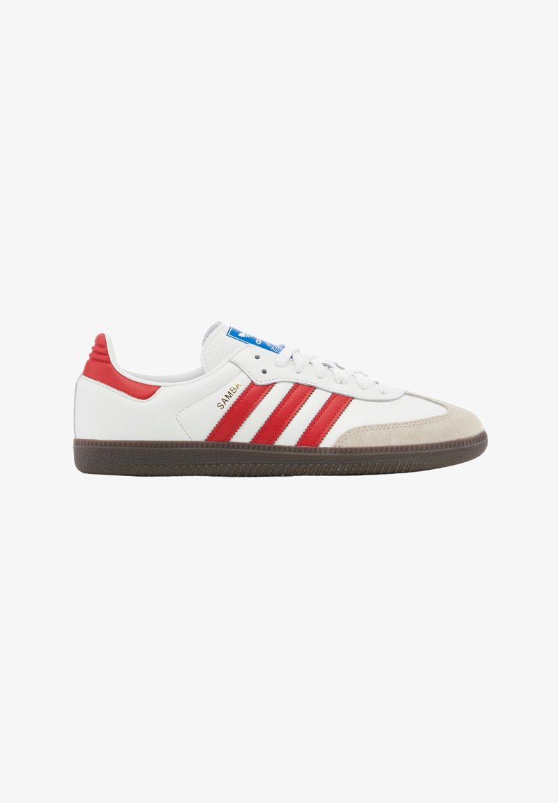 Vit Adidas Samba-sneaker med röda ränder, röd hälflik, beige mocka tåkappa och brun gummisula, sidovisning.