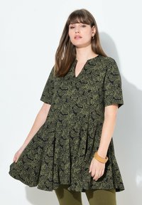 Vestido de patrones verdes y negros con mangas cortas, escote en V y silueta acampanada; combinado con una pulsera ámbar.