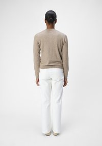 Lys brun genser med lange ermer. Kombinert med hvite, vide bukser. Enkel design, myk tekstur, minimal detaljering.