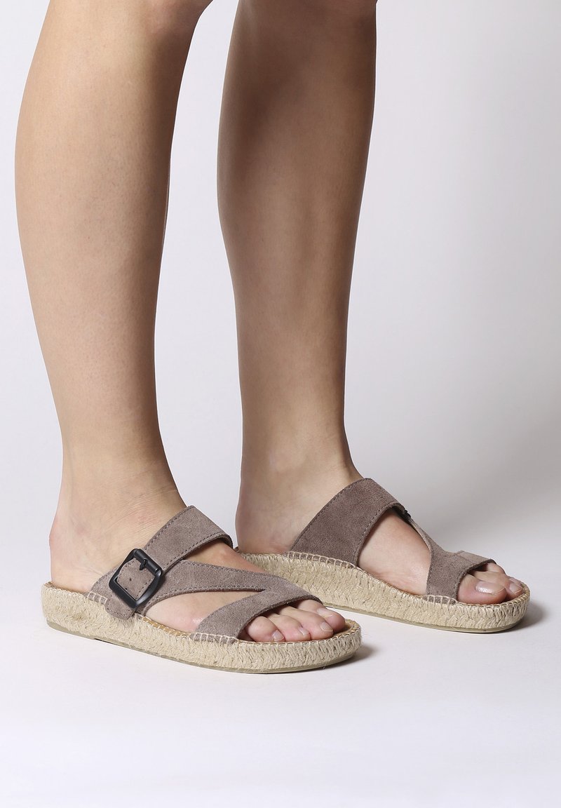 Sandali incrociati in suede marrone con suola pianeggiante in espadrillas, dotati di un accentuato cinturino nero e design open-toe.
