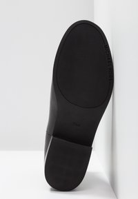 Semelle d’une chaussure habillée noire Michael Kors avec une zone de prise texturée et la taille 5½M visible, positionnée sur un fond blanc.