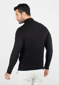 Pull noir à manches longues avec un col montant, au design épuré, texture en maille fine et poignets côtelés, vu de dos.
