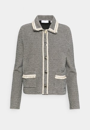 Veste à carreaux noir et blanc avec un col, poches avant, bordure crème contrastante et cinq boutons de fermeture. Texture tissée lisse.