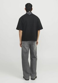 Svart oversized t-shirt med kort ärm och fyrkantig form, i kombination med lösa grå denimbyxor som har bakfickor och minimal detaljering.
