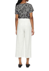 Top a maniche corte con motivo in bianco e nero, dal fit ampio, abbinato a pantaloni bianchi a gamba larga a vita alta, con due tasche posteriori.