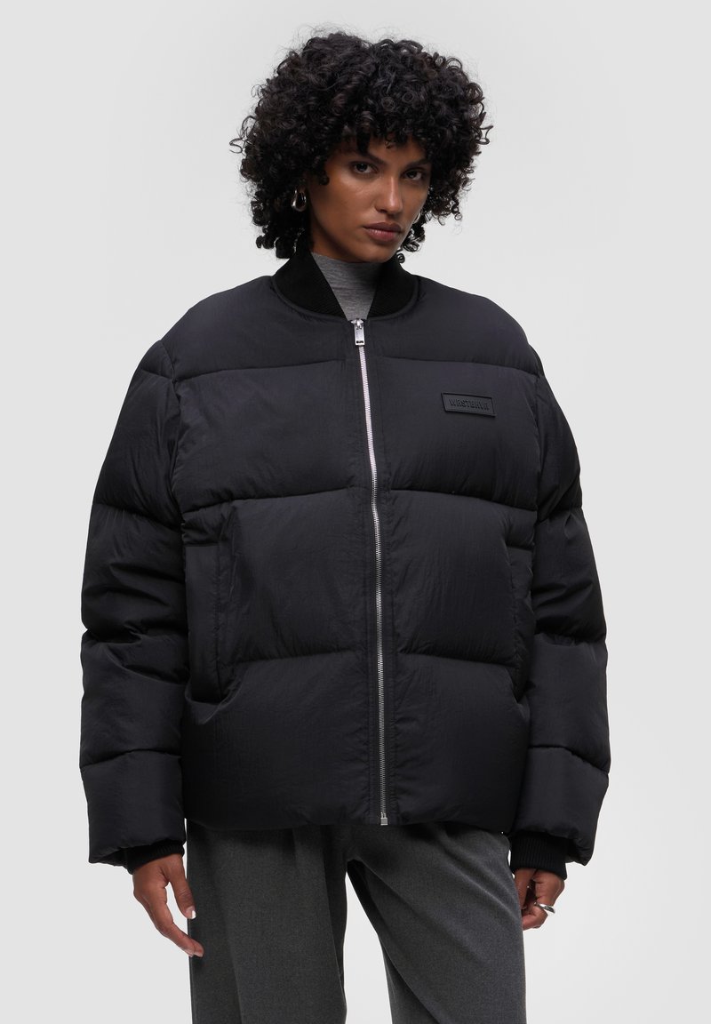 Czarna kurtka puchowa z zapięciem na zamek, z dużymi pikowanymi sekcjami, wysokim kołnierzem i małą metką z logo na piersi.