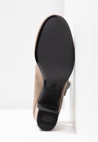 Bottine beige en daim reposant contre une surface blanche, montrant une semelle noire lisse avec un motif antidérapant et une pointure 37.