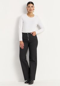 Mungkin jeans hitam tinggi dengan lima kancing perak, saku samping, dan potongan kaki lurus, dipadukan dengan atasan lengan panjang putih.