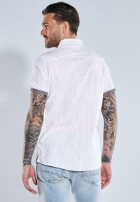 Kurzarm, weißes Leinenhemd mit einem subtilen Streifenmuster. Verfügt über einen grauen Saum an den Ärmeln und einen geraden Saum.