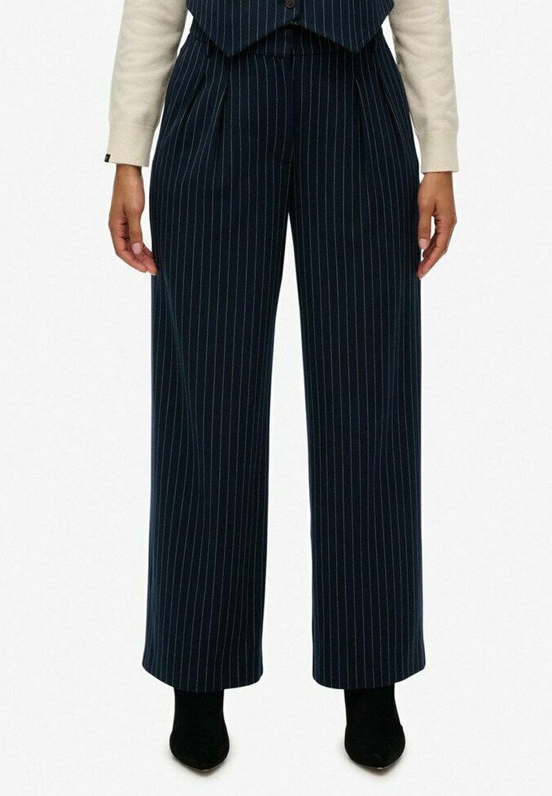 Pantaloni a gamba larga in navy con righe sottili, con frontale plissettato, realizzati in tessuto leggero, caratterizzati da una vita alta e abbinati a décolleté nere.
