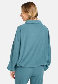 Modrý žebrovaný top s dlouhým rukávem, který má volný střih, oversized siluetu a límec; kombinovaný s odpovídajícími kalhotami, které vykazují texturovanou tkaninu.