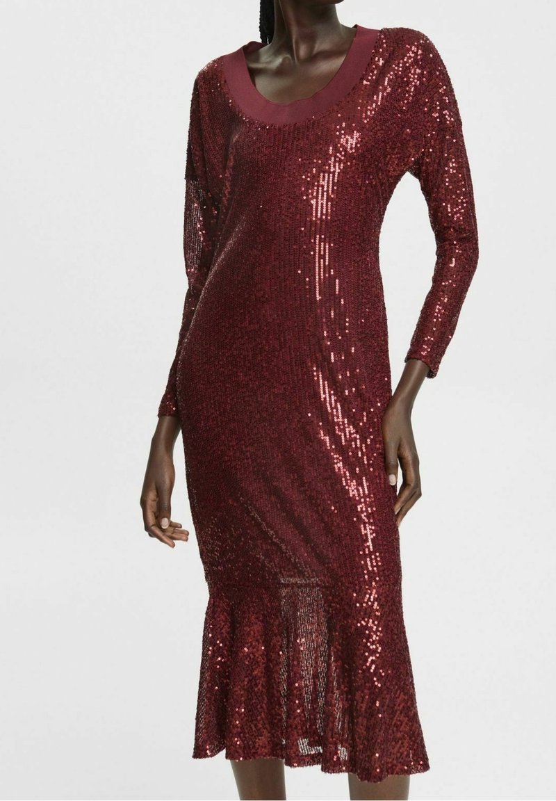 Burgunderfärgad klänning med paljetter, lång ärm, rundad halsringning och utsvängd nederkant. Tyget har en glänsande yta som reflekterar ljus.