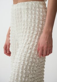 Weiße, strukturierte Hose mit einer Reihe von erhobenen, wellenförmigen Mustern, ausgestattet mit einem elastischen Bund und einer lockeren Passform.