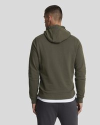 Un hoodie vert olive avec une capuche à cordon de serrage, des poignets côtelés et un ourlet droit. Fabriqué en tissu doux, porté sur une chemise blanche et un pantalon gris.