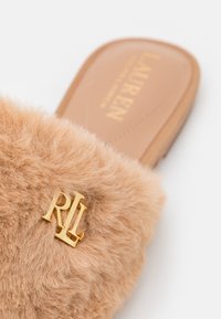 Claquette en fausse fourrure beige avec une texture douce, arborant un accent doré "RL" sur la bride et une semelle intérieure lisse marron.
