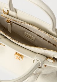 Τσάντα χειρός από κρεμ δέρμα με χρυσό φερμουάρ, εσωτερική τσέπη με φερμουάρ και ετικέτα Tommy Hilfiger στο εσωτερικό.