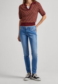 Gestreepte bordeauxrode trui met korte mouwen en een kraag, gecombineerd met blauwe skinny jeans en zwarte sneakers met witte zolen.