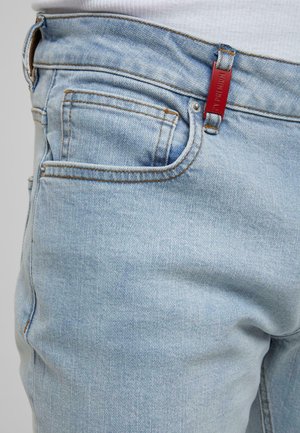 Světlé modré džíny z denimu s oranžovým prošíváním a malou červenou obdélníkovou cedulkou připevněnou na pásku blízko přední kapsy.