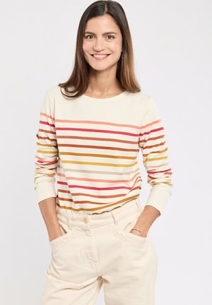 Lange mouw crèmekleurig top met meerkleurige strepen in roze, oranje en bruin, gecombineerd met lichtgekleurde broeken. Heeft een ronde halslijn en aansluitende mouwen.