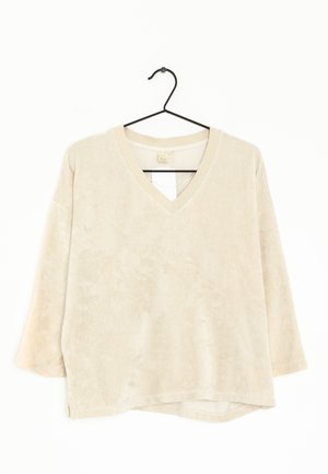 Sweatshirt beige à col en V avec manches longues, texture douce et ourlet légèrement asymétrique. Conçu avec des accents en boucle de tissu au niveau de l'encolure.