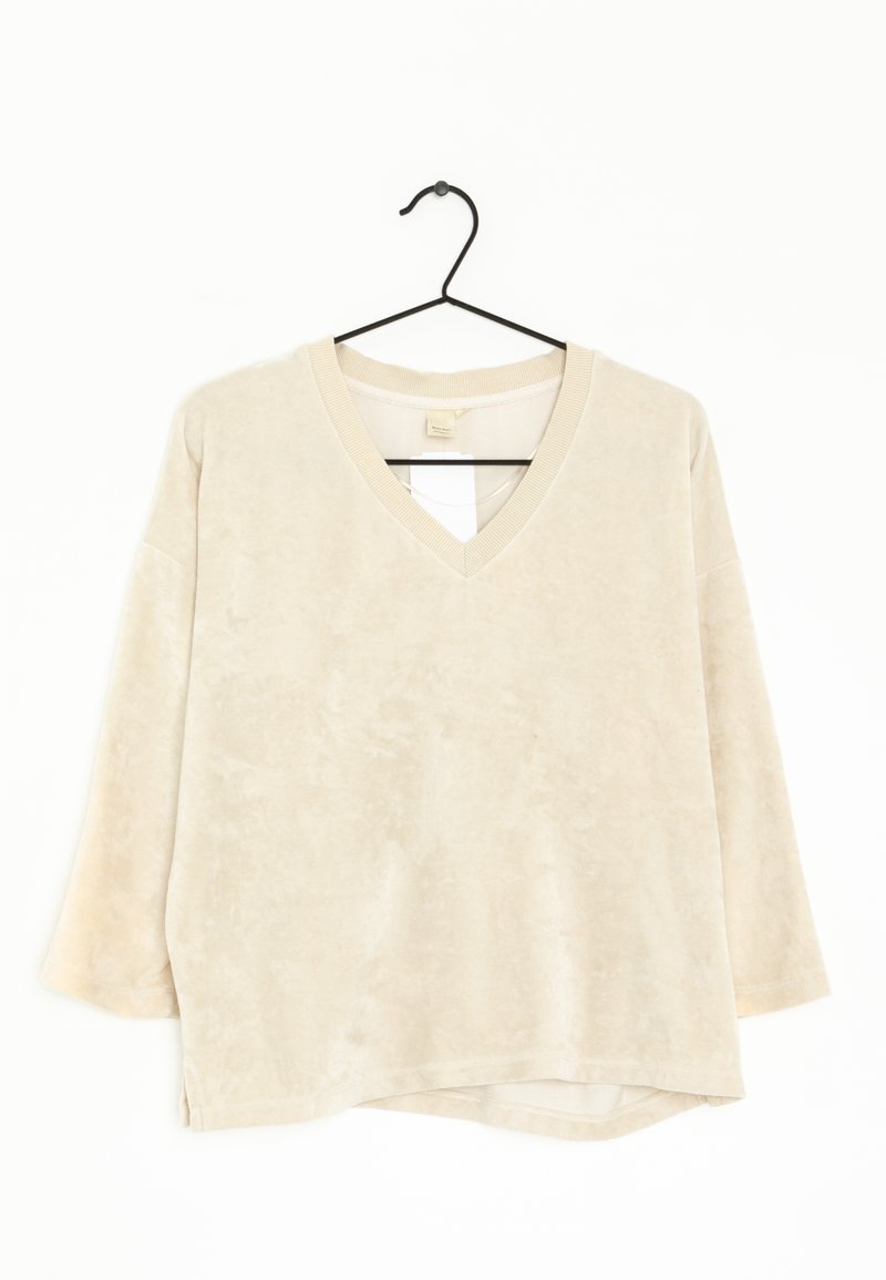 Beige V-neck sweatshirt with long sleeves, soft texture, and a slight hi-low hem. Designed with fabric loop accents at the neckline.